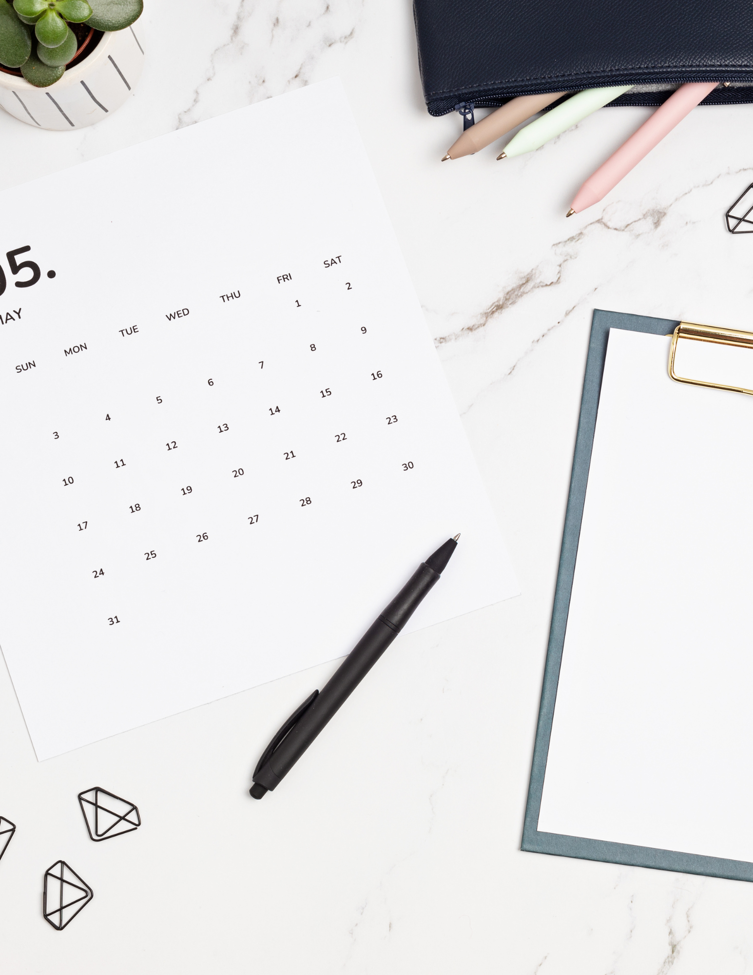 A monthly calendar, planner, and pens laid out on a marble desk